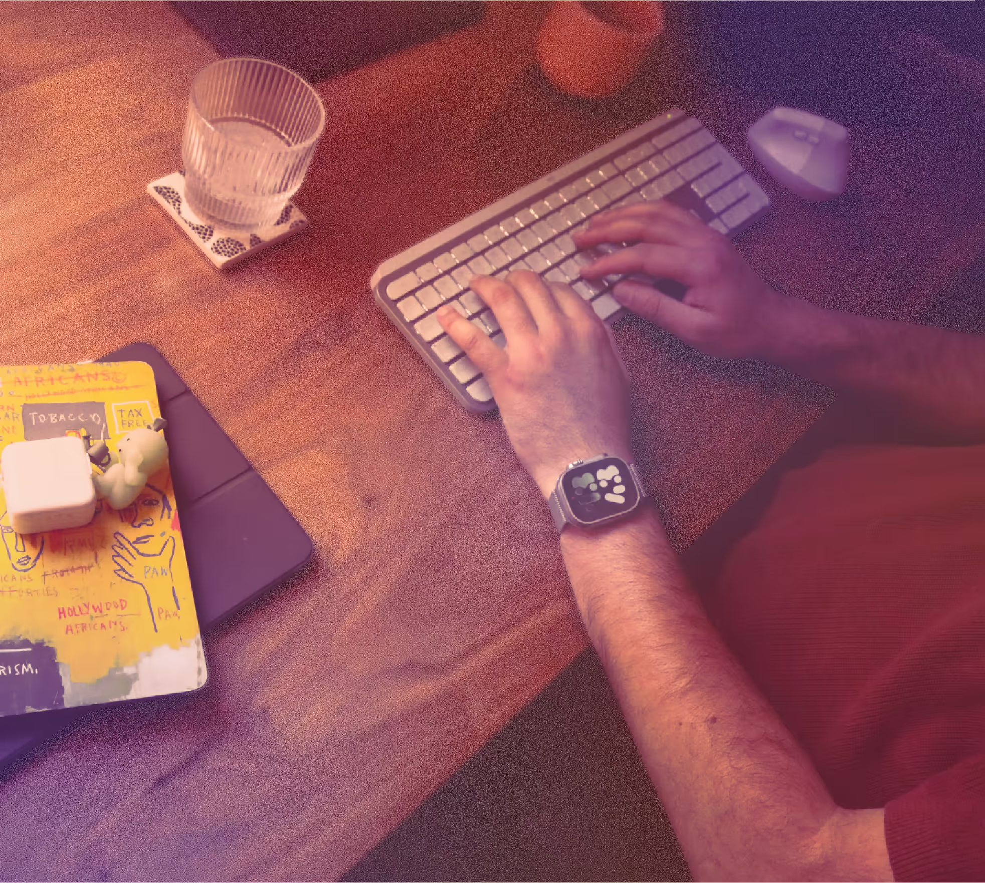 Person typing on a wireless keyboard with a smartwatch visible and items on a wooden desk.
