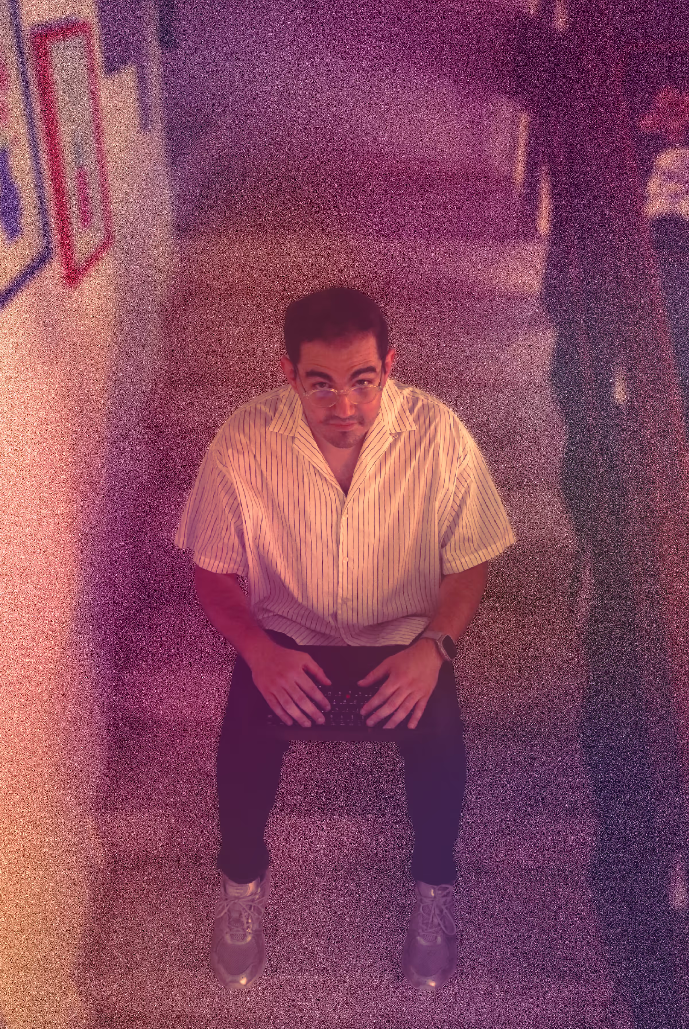 Man with glasses sitting on stairs holding a keyboard, looking up at the camera.