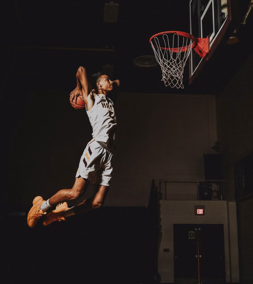 Basketball player in mid-air about to dunk toward a hoop in an indoor gym.