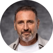 Middle-aged man with short hair and a trimmed beard wearing a white shirt and light jacket, smiling slightly against a gray background.