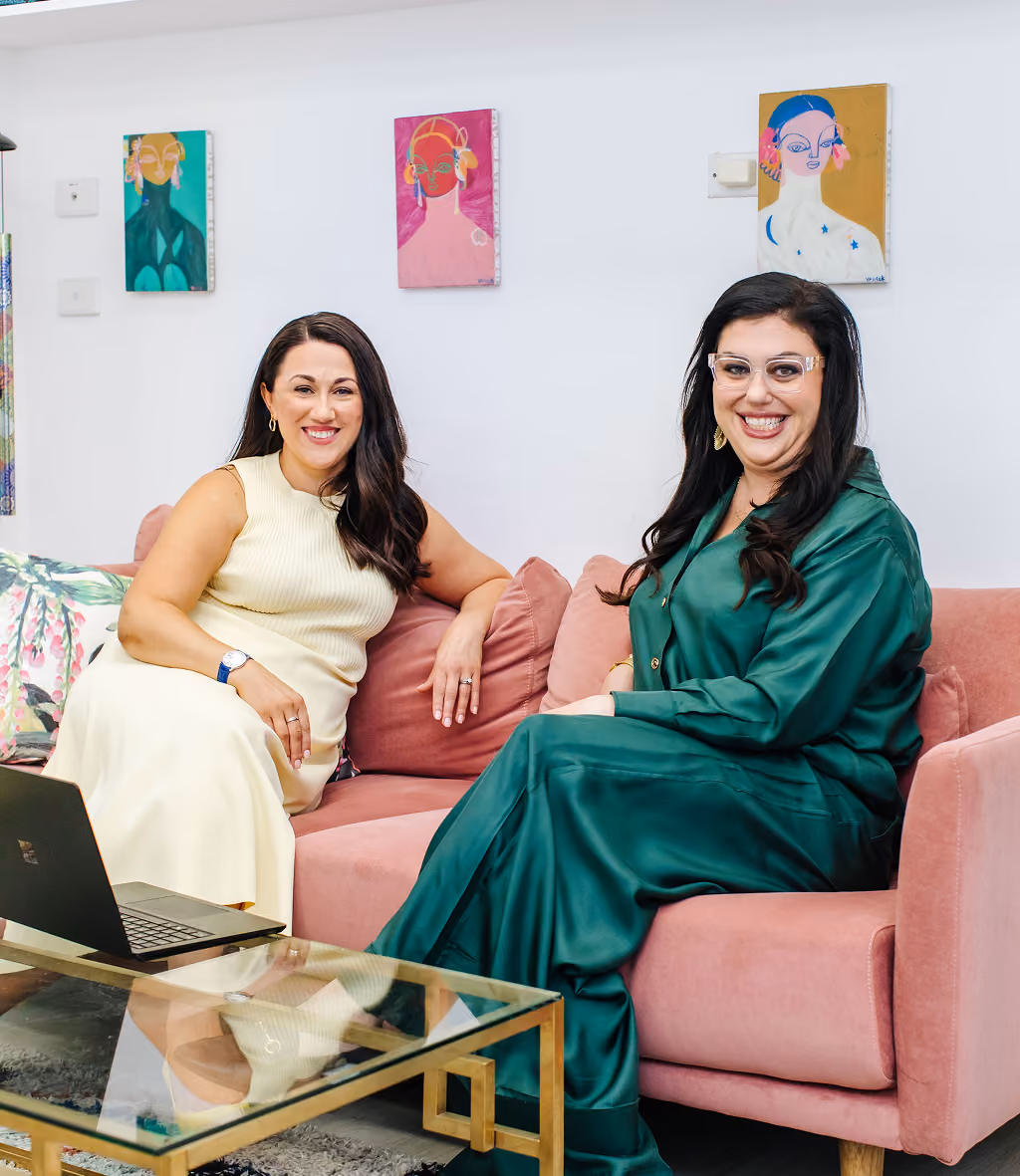 The co-owners of Respect Wills and Estates, Nadya and Danielle, sitting on a couch smiling.