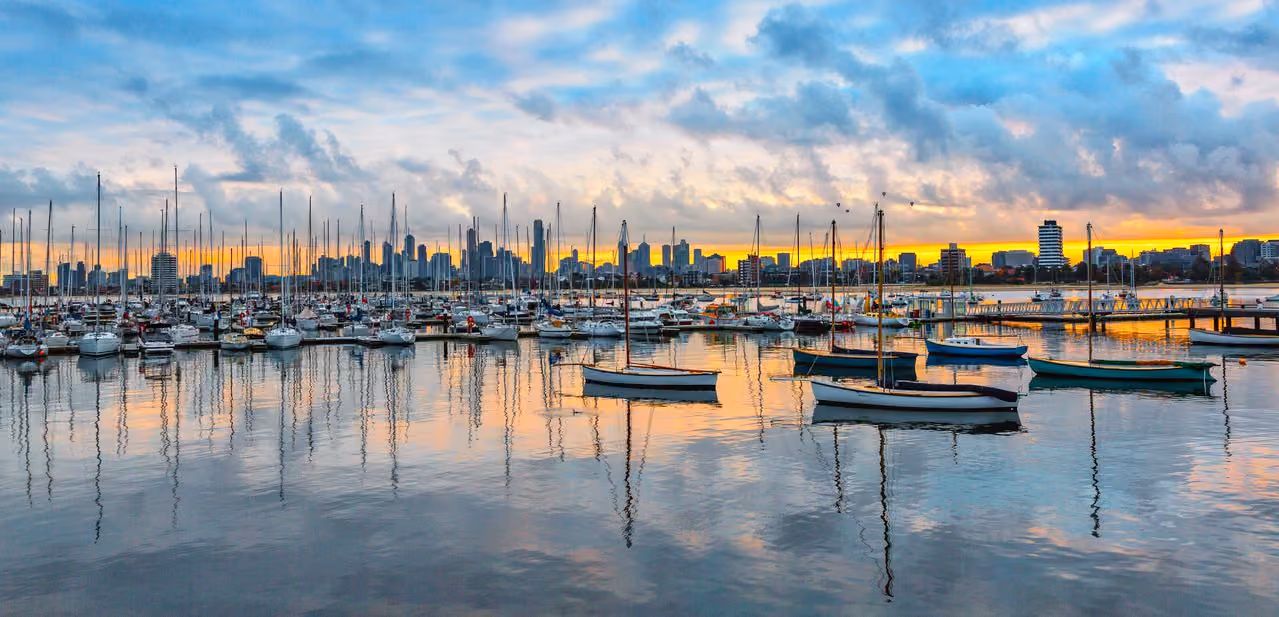 A picture of sailboats by the docks with the Melbourne sunset in the background.