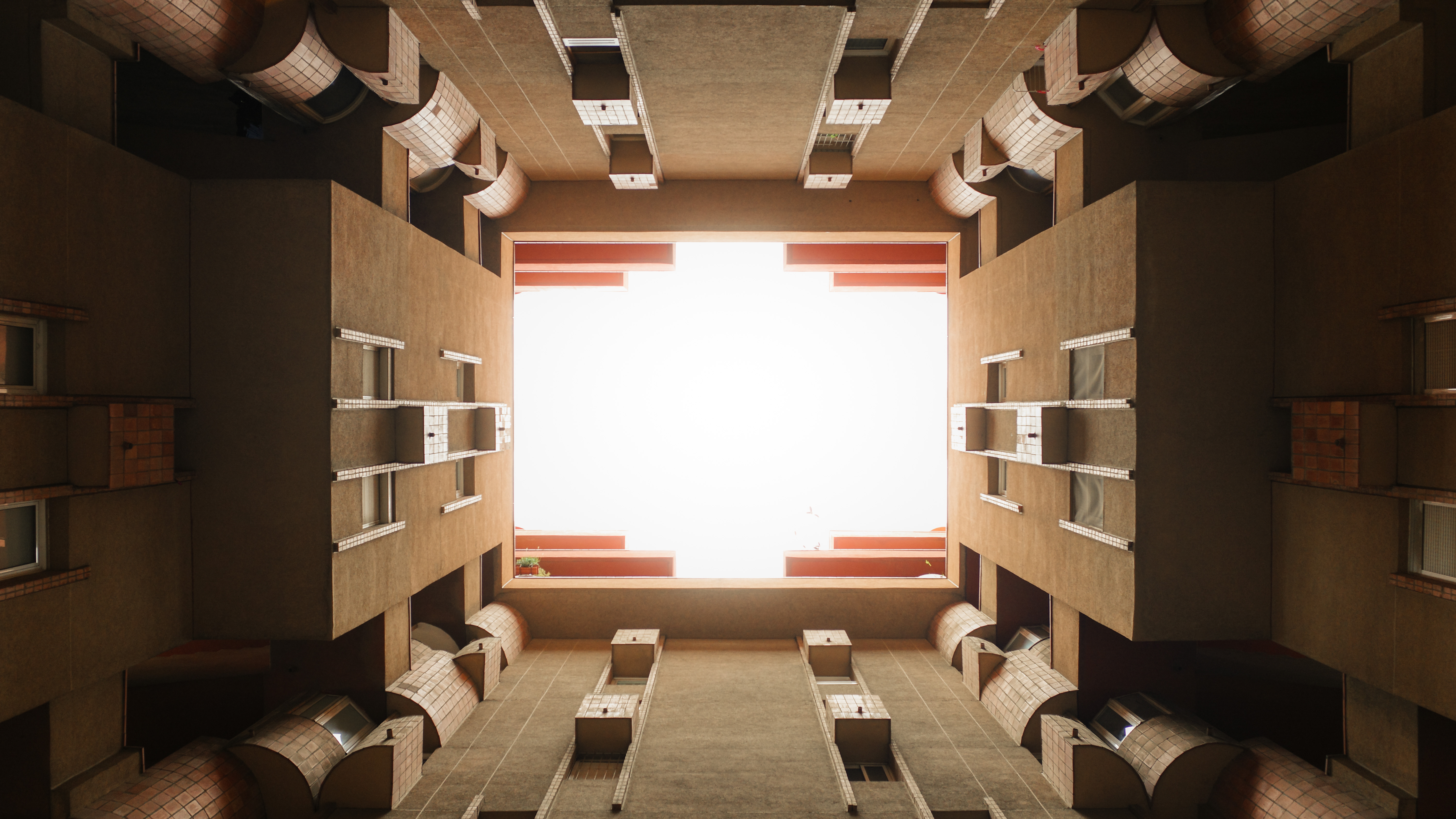 View looking up inside a square courtyard surrounded by brown building walls and windows.