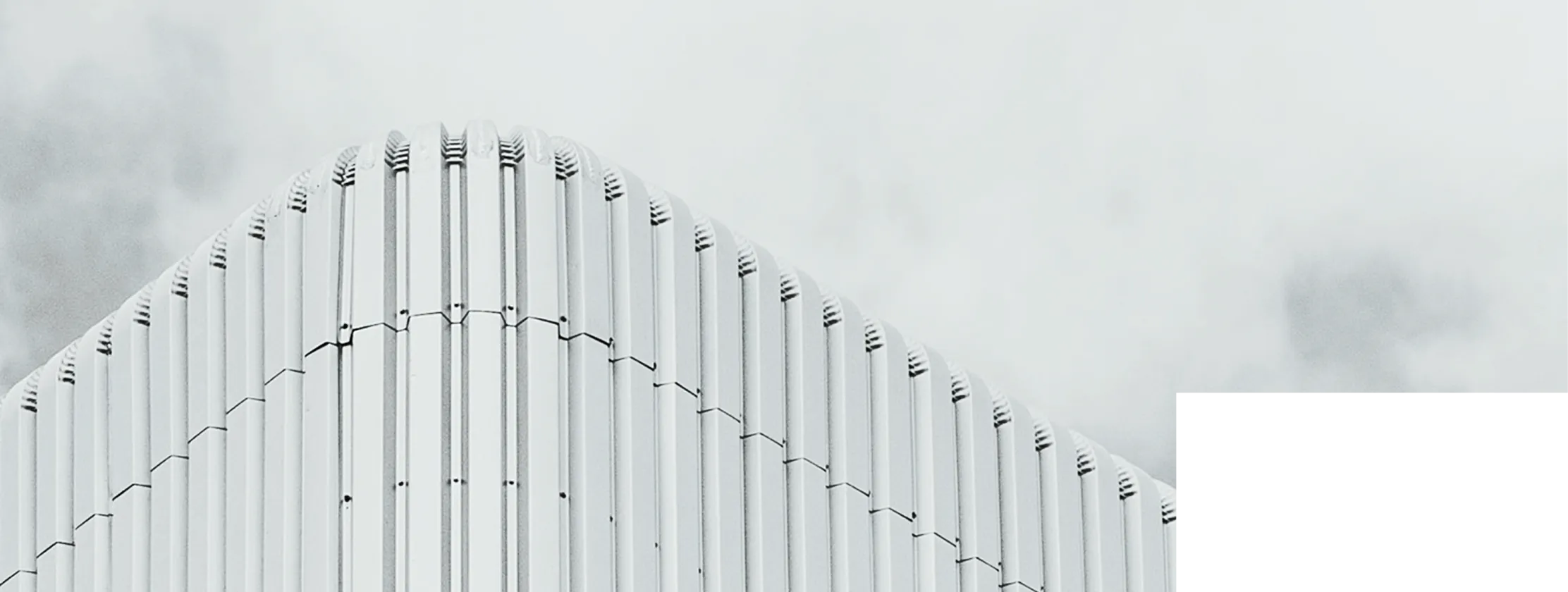 A modern white building with vertical fins and a curved roofline against a cloudy sky.