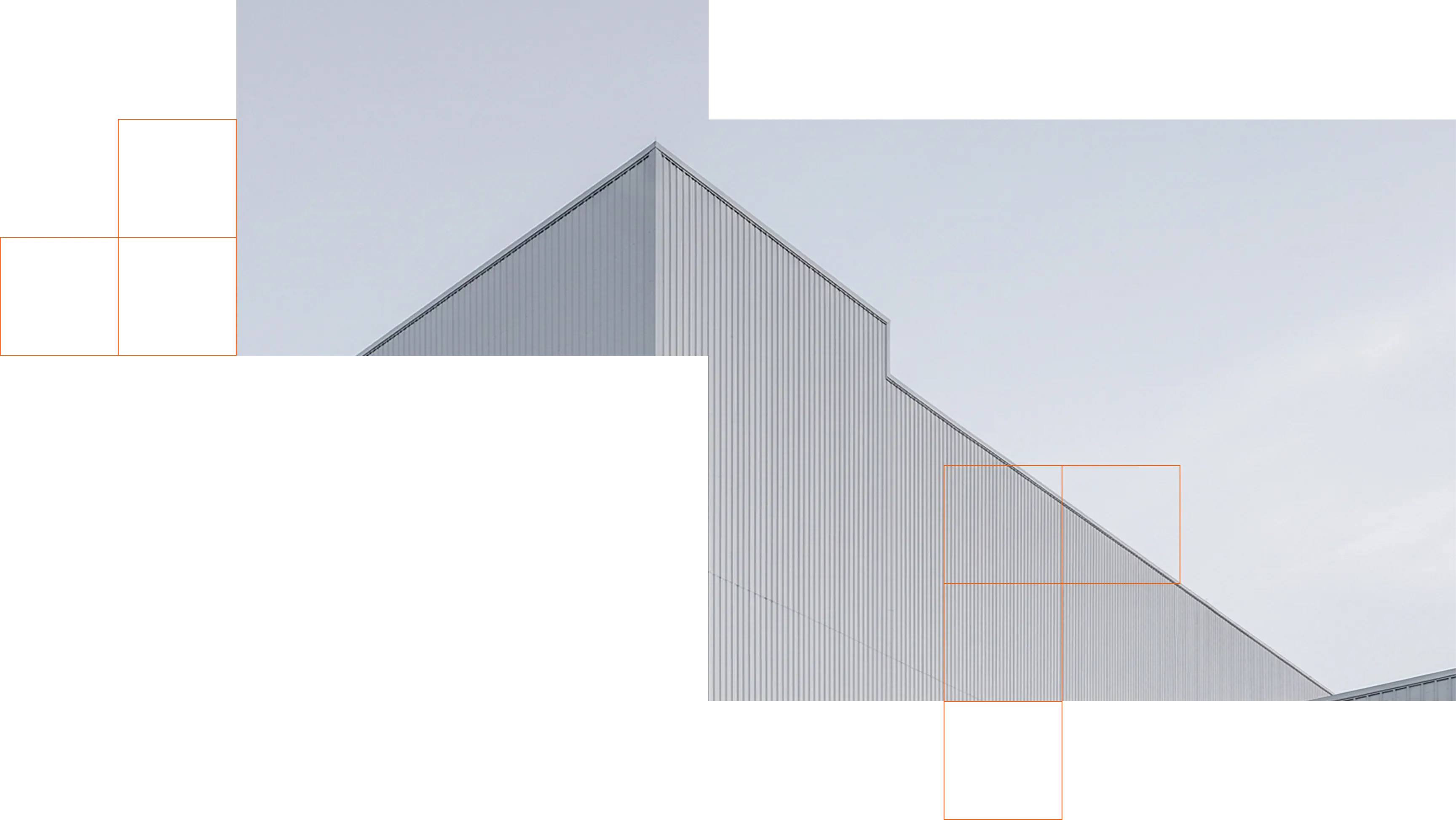 A modern gray corrugated metal building with a steep gabled roof and sloping side wall against a pale sky.