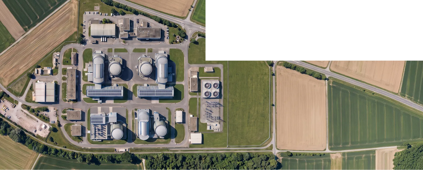 An aerial view of an industrial facility with multiple cylindrical storage tanks and processing buildings, surrounded by farmland and roads.