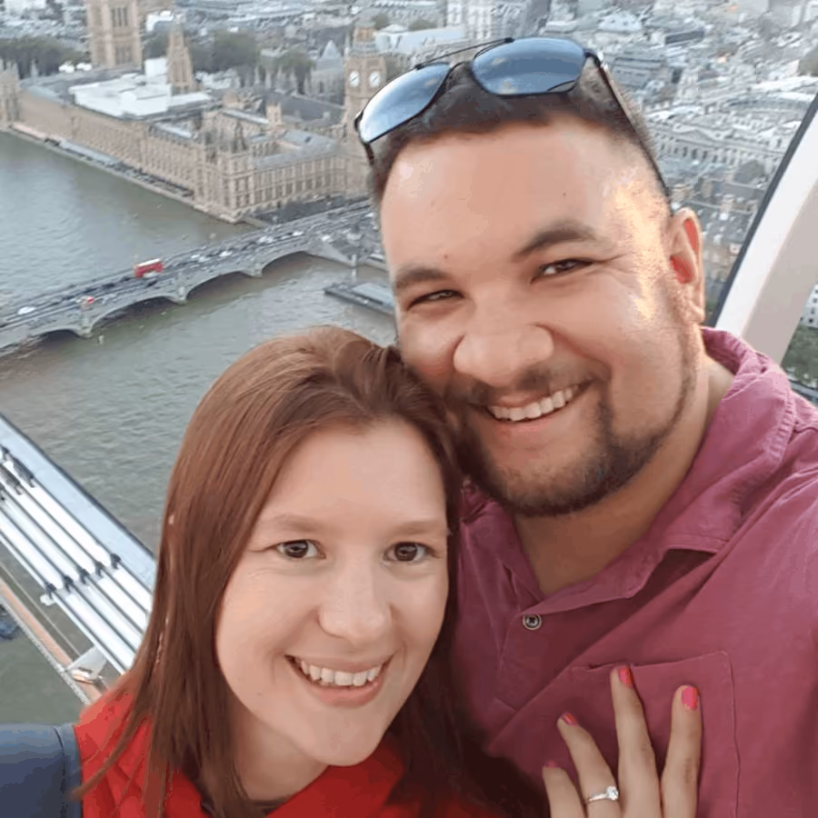 Smiling couple taking a selfie with River Thames and Houses of Parliament in the background.