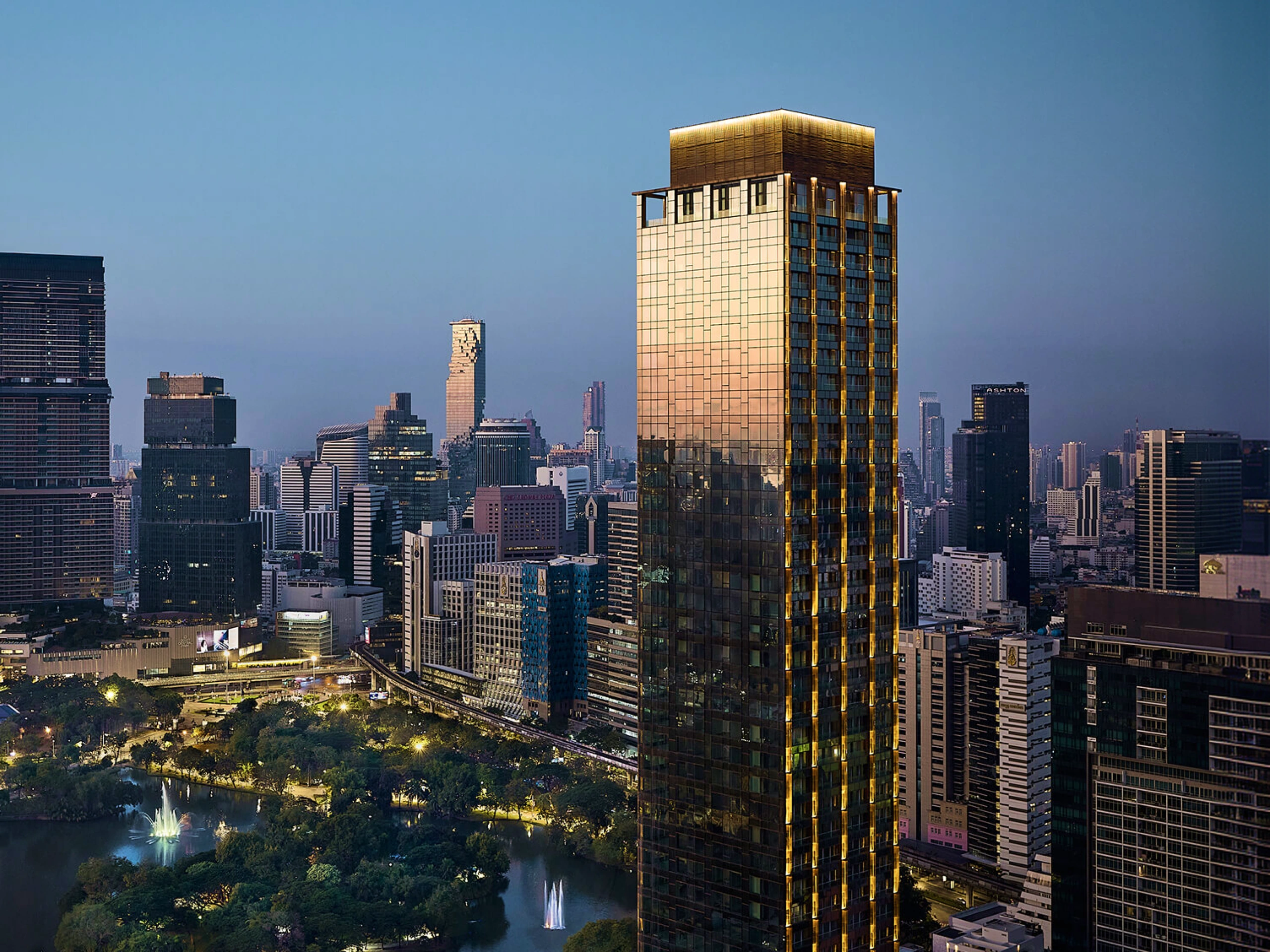 NIMIT Lumpini Park North tower rising above Lumpini Park and the Bangkok skyline at dusk