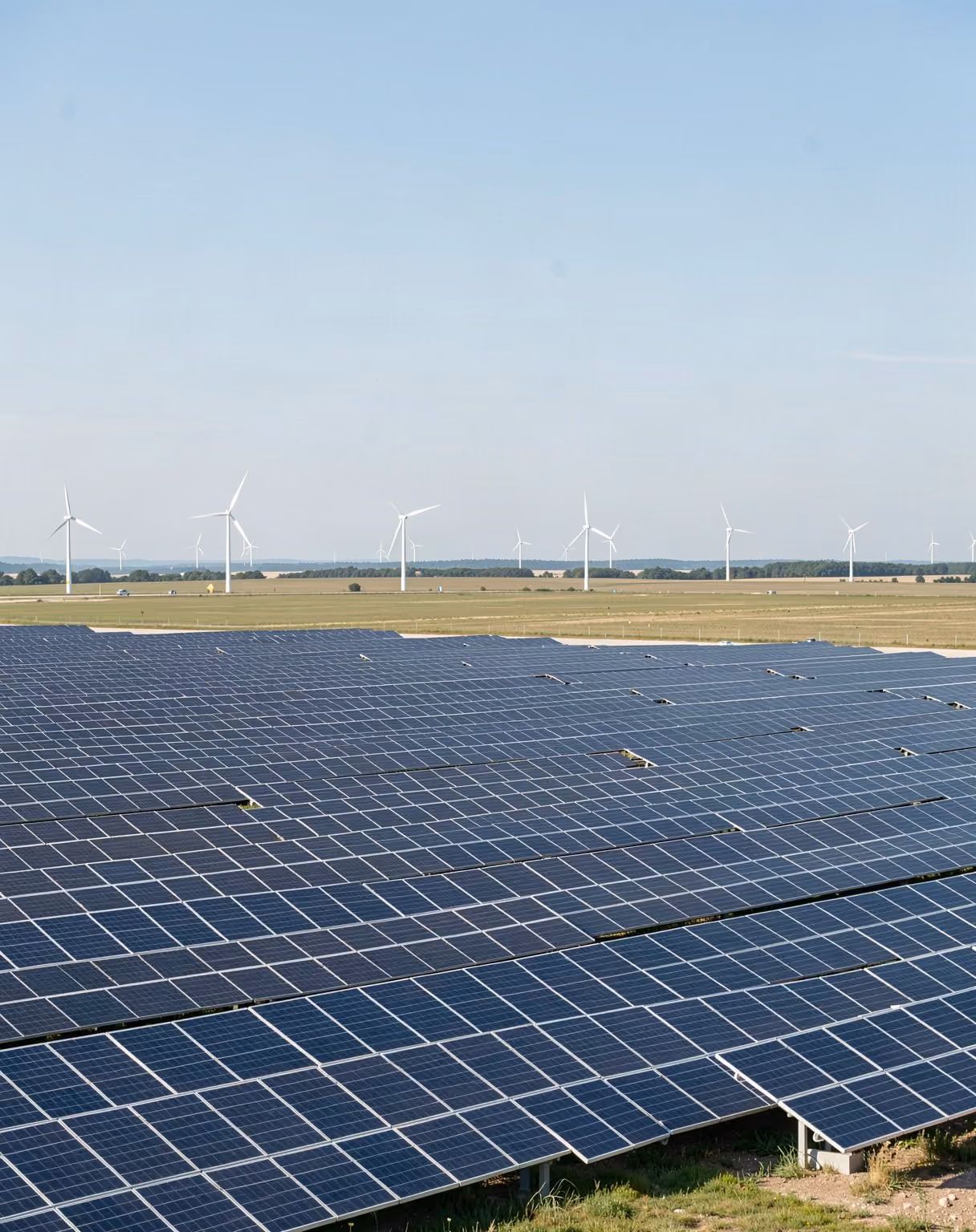 Rows of solar panels with wind turbines on the horizon