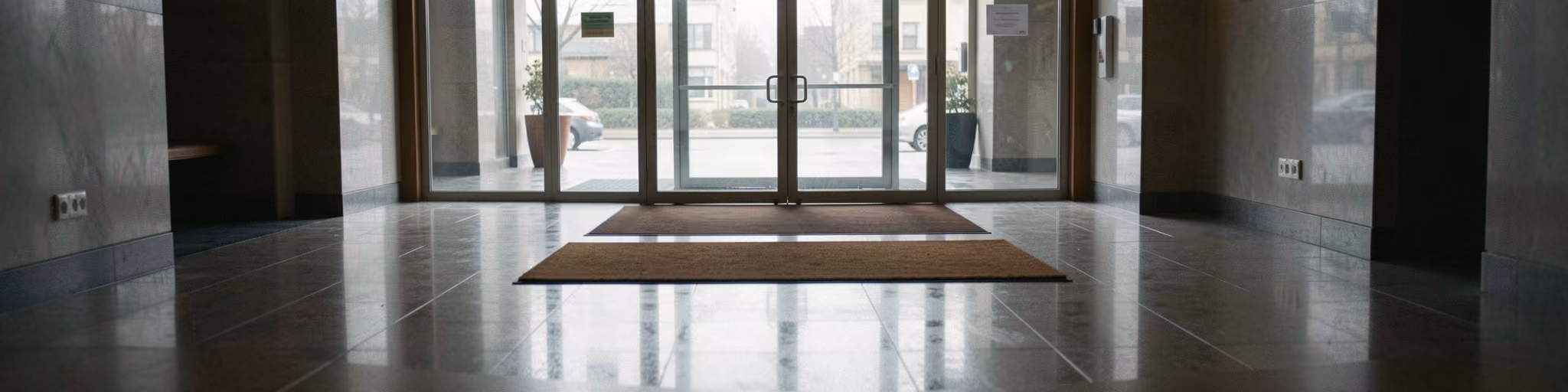A polished lobby floor with an entrance mat and glass doors