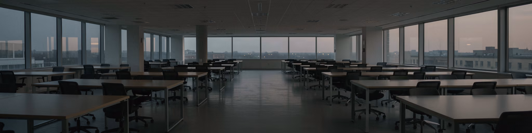 An empty open-plan office of vacant desks and chairs at dusk