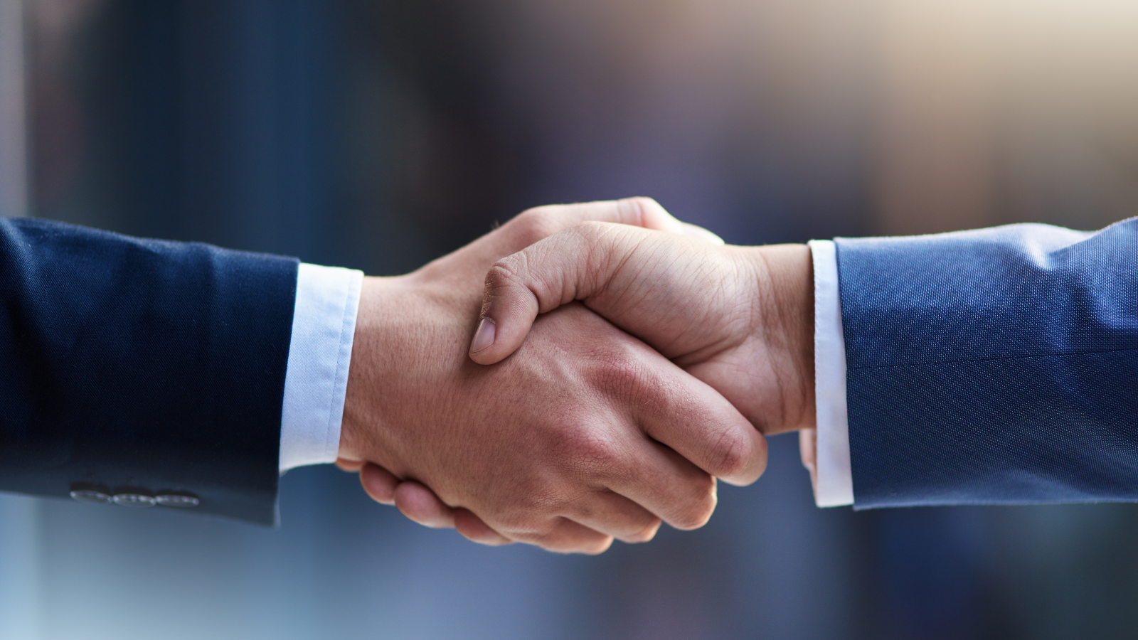 Close-up of two people in business suits shaking hands in a professional setting.