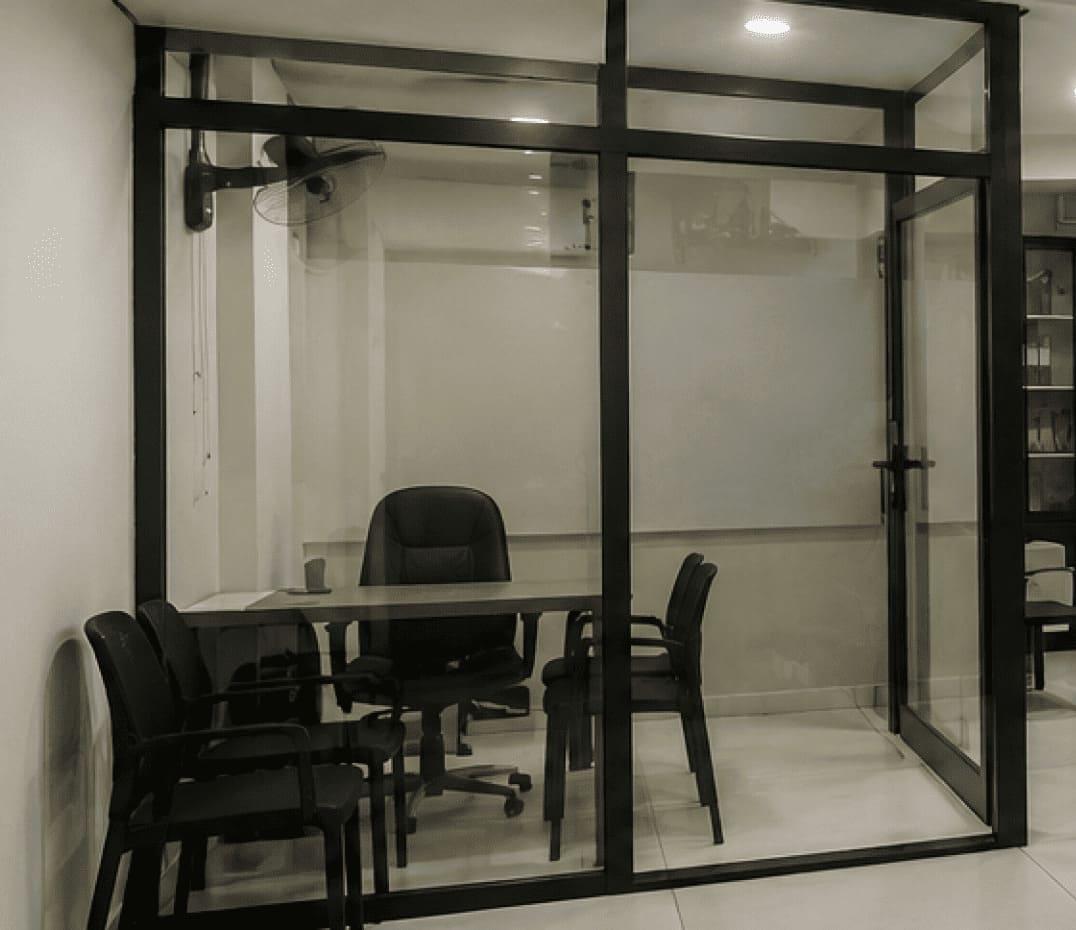 Glass-walled office with a desk, a black swivel chair, and four black visitor chairs.
