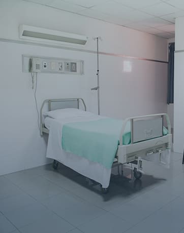 Empty hospital bed with green blanket and white sheet in a clean, white-walled room.