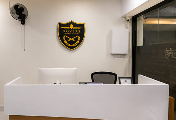 Reception desk in an office with a Rovers Security Services shield logo on the wall and a black chair behind it.