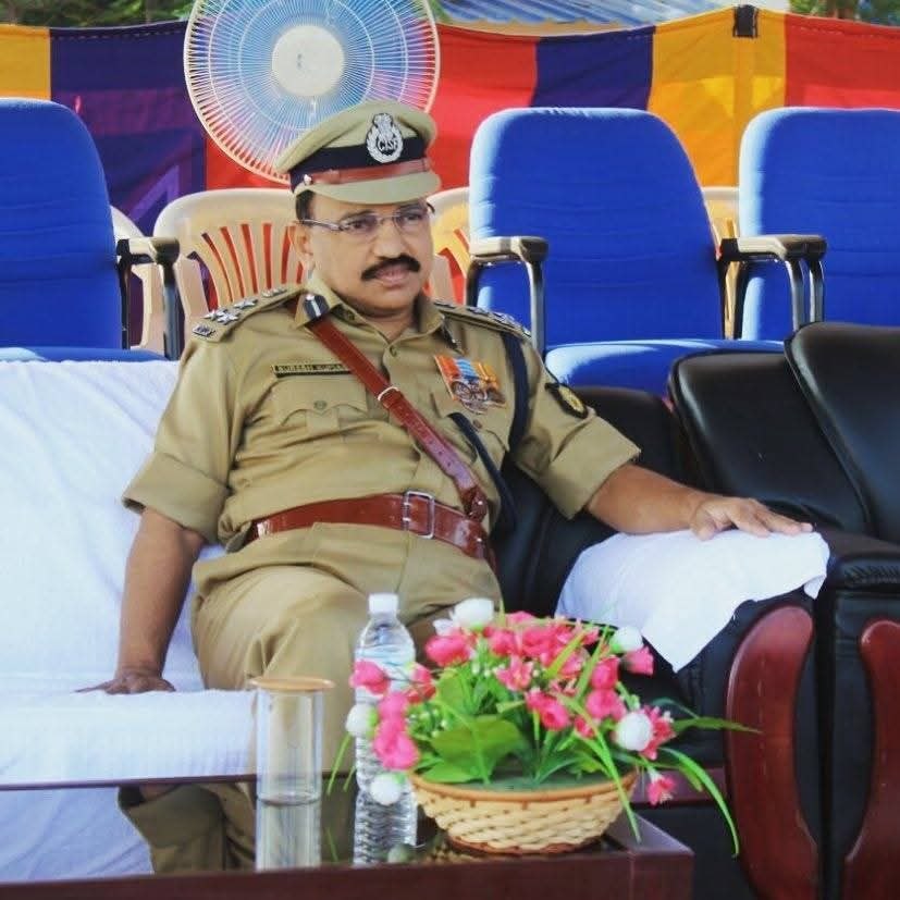 Uniformed police officer with medals sitting on a white-covered chair at a formal outdoor event.