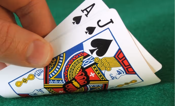 Hand holding playing cards showing ace and jack of spades on green felt surface.