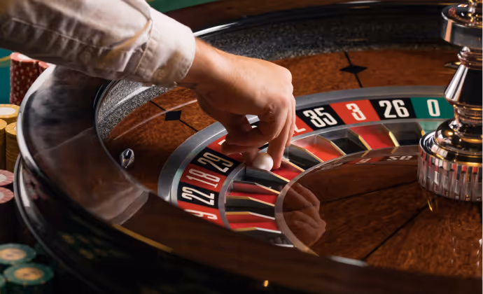 Hand placing white ball on a roulette wheel numbered with red, black, and green pockets.