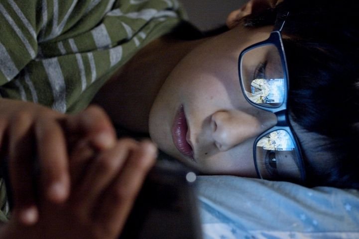 person struggling to fall asleep while using a smartphone in bed
