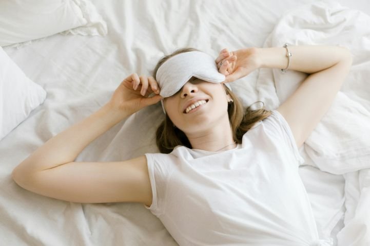 A smiling woman wearing a sleep mask after getting good, quality sleep.