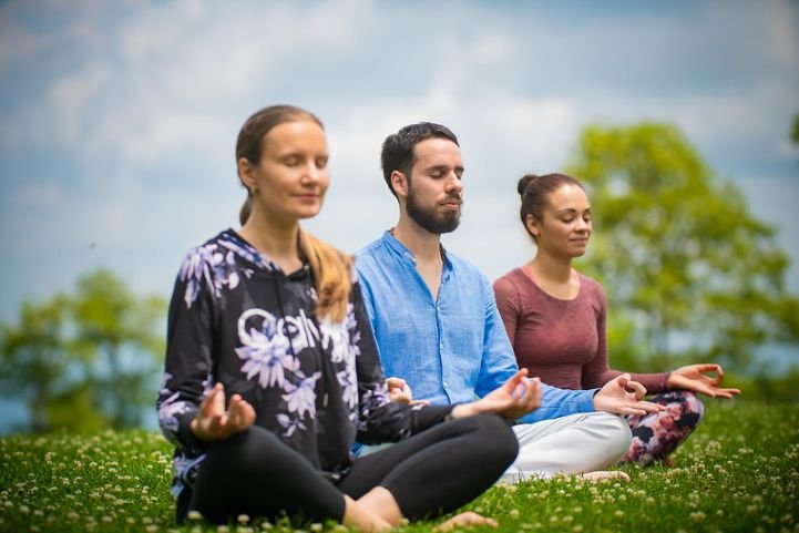 Two women and a man practicing SKY Breath Meditation sitting on the grass.