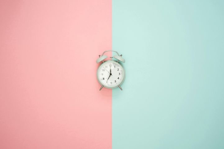 An old-fashioned alarm clock with a pink and mint split screen depicting time management and life balance.