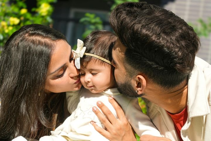 Loving parents practicing positive parenting while kissing their child's cheeks.