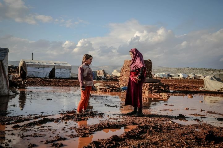 A woman and a female child are standing in the middle of a refugee camp following a traumatic event.