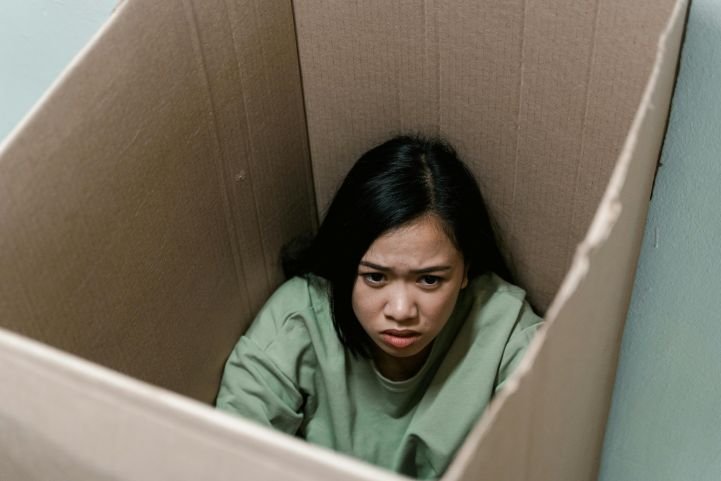 A young woman sitting in a box, feeling depleted following a panic attack.
