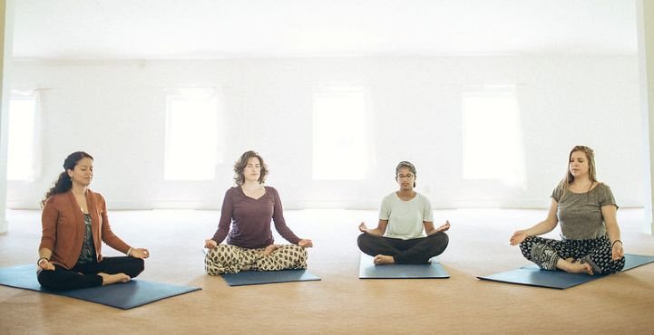 Four young women sitting on yoga mats and practicing SKY on an Art of Living Part 1 Course.