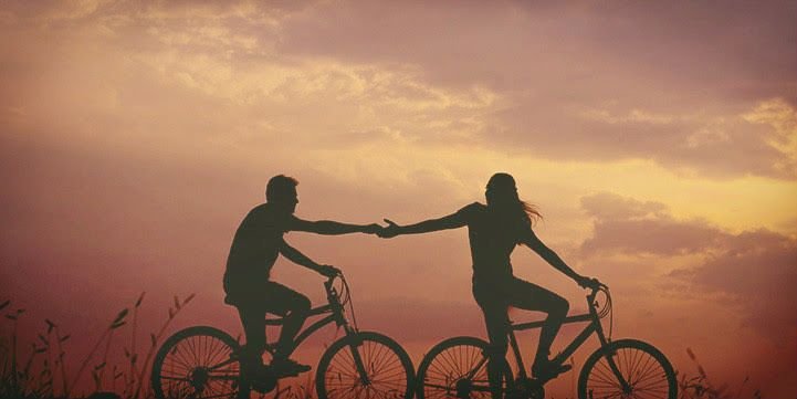 A couple riding bicycles at sunset.
