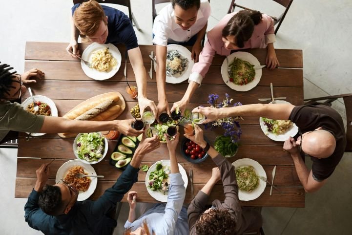 Overhead view of a table with friends connecting over healthy foods, cheering to good mental health.