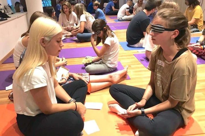 Two females are sitting together, one is practicing reading with a blindfold on an Intuition Process course.