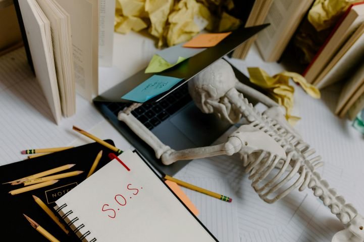 A skeleton hunched over a laptop next to an SOS signifying modern world challenges.