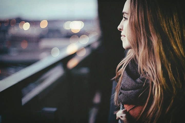 A calm, reflective woman looking out a window while enjoying a regulated nervous system.