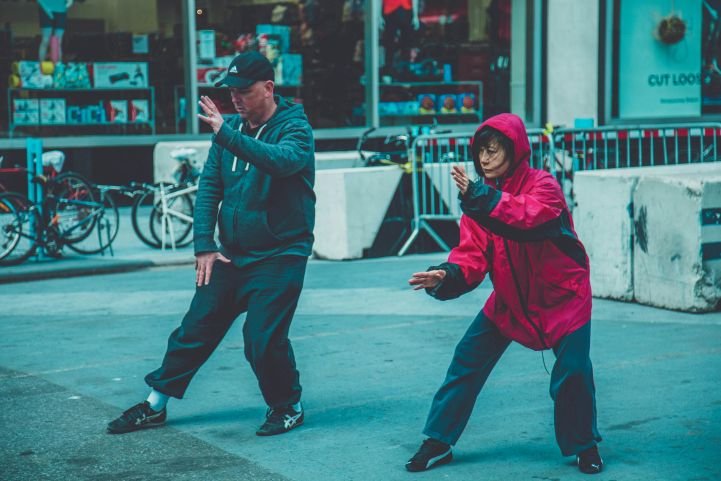 A man and a woman practicing Tai Chi on a city street.