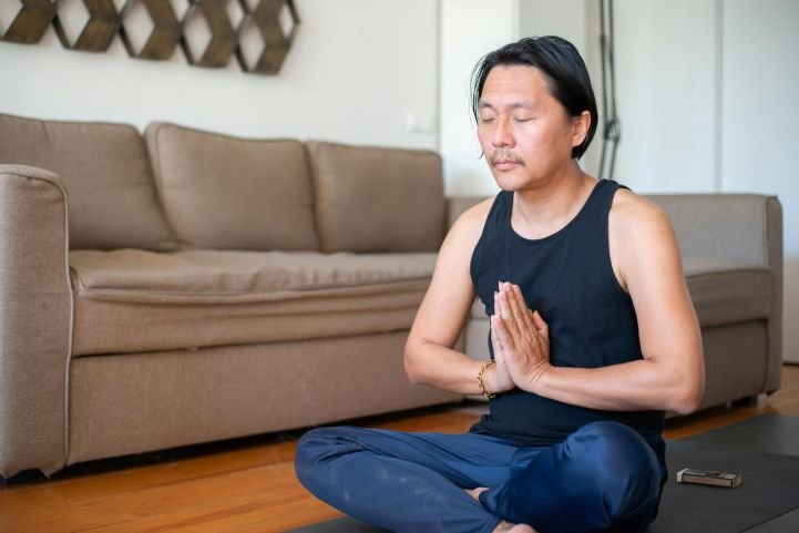 Man practicing the anjali mudra on a yoga mat at home.