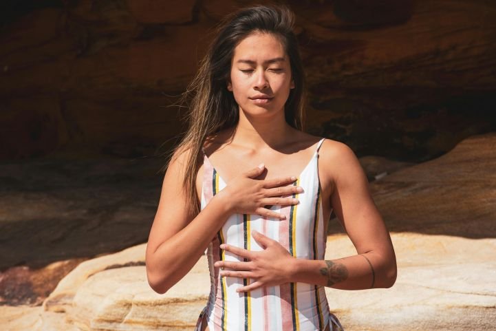 Young woman with her hands resting on her chest and stomach, while practicing breath awareness.