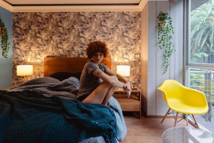 Young woman stuck in her thoughts, sitting on the edge of a bed.