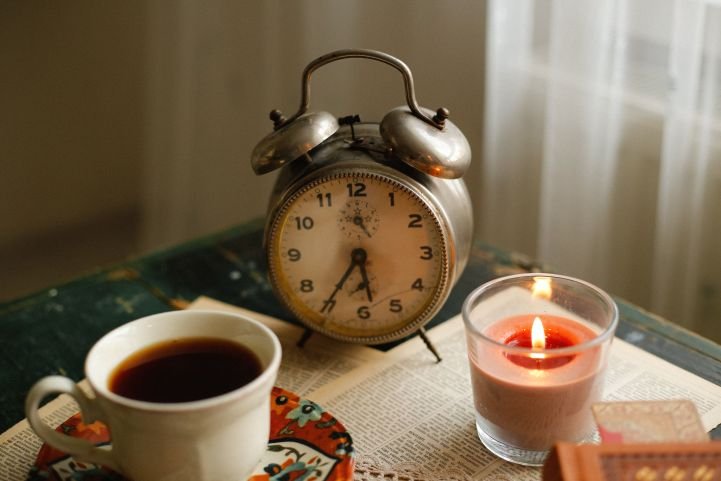 A cup of tea and a candle in front of an old-style alarm clock.