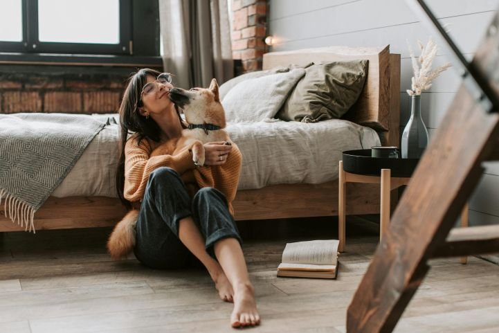 Relaxed woman sitting on the floor next to her bed, after practicing the Sleep and Anxiety Protocol, enjoying the moment with her dog.