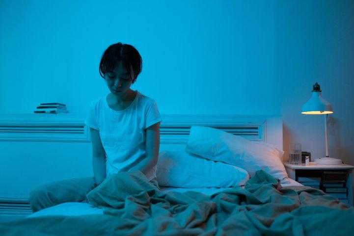 Woman sitting on the edge of her bed, tired but wired and unable to sleep.