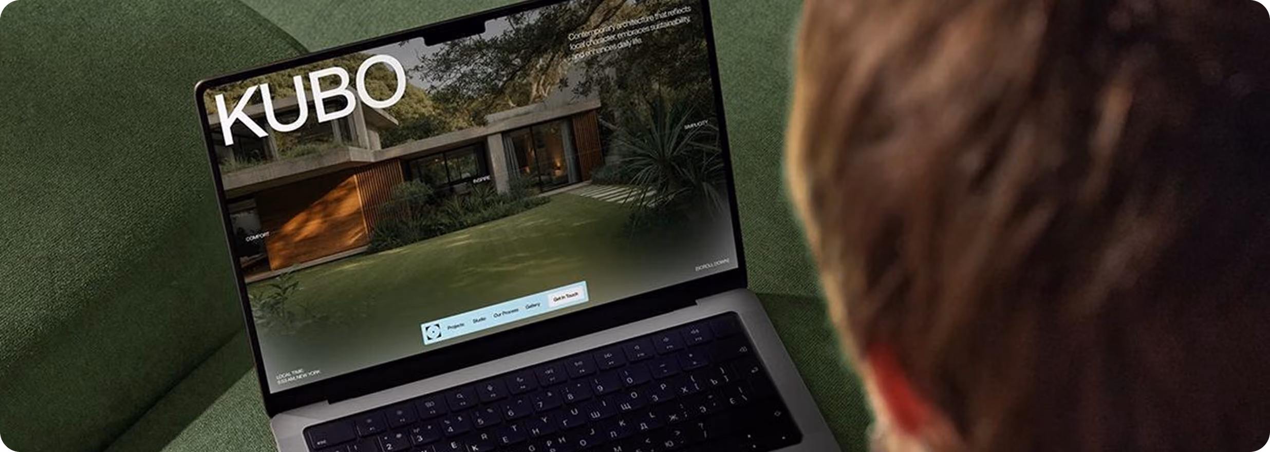 Person viewing a laptop screen displaying a website with the title KUBO featuring a modern house surrounded by greenery.