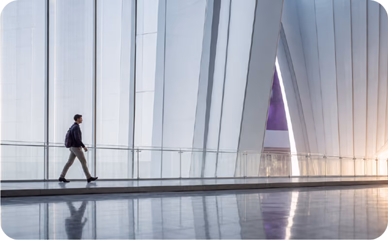 Man with backpack walking inside a modern building with tall white vertical panels and reflective floor.