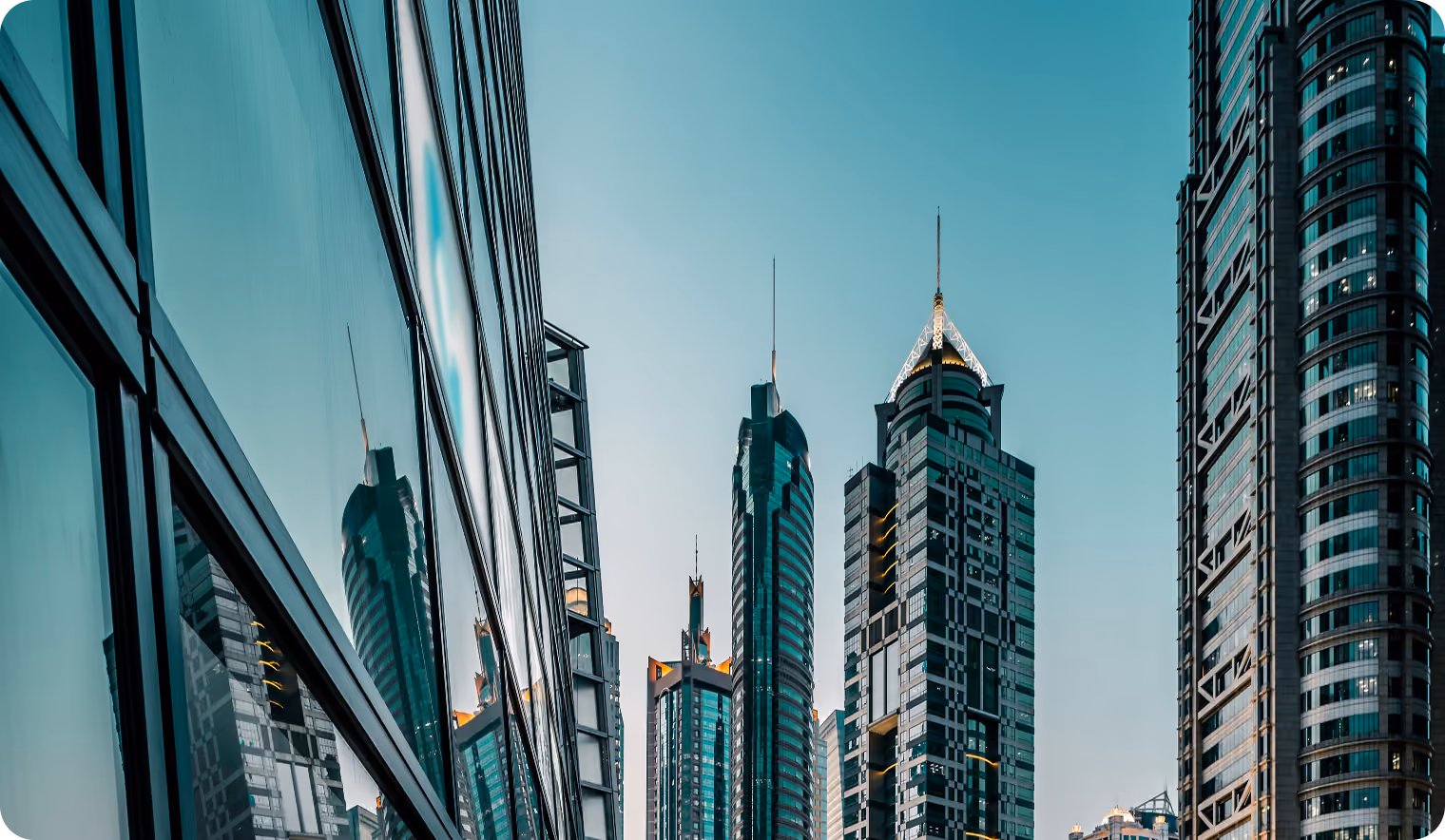 Modern skyscrapers with glass facades reflecting each other under a clear sky in an urban setting.