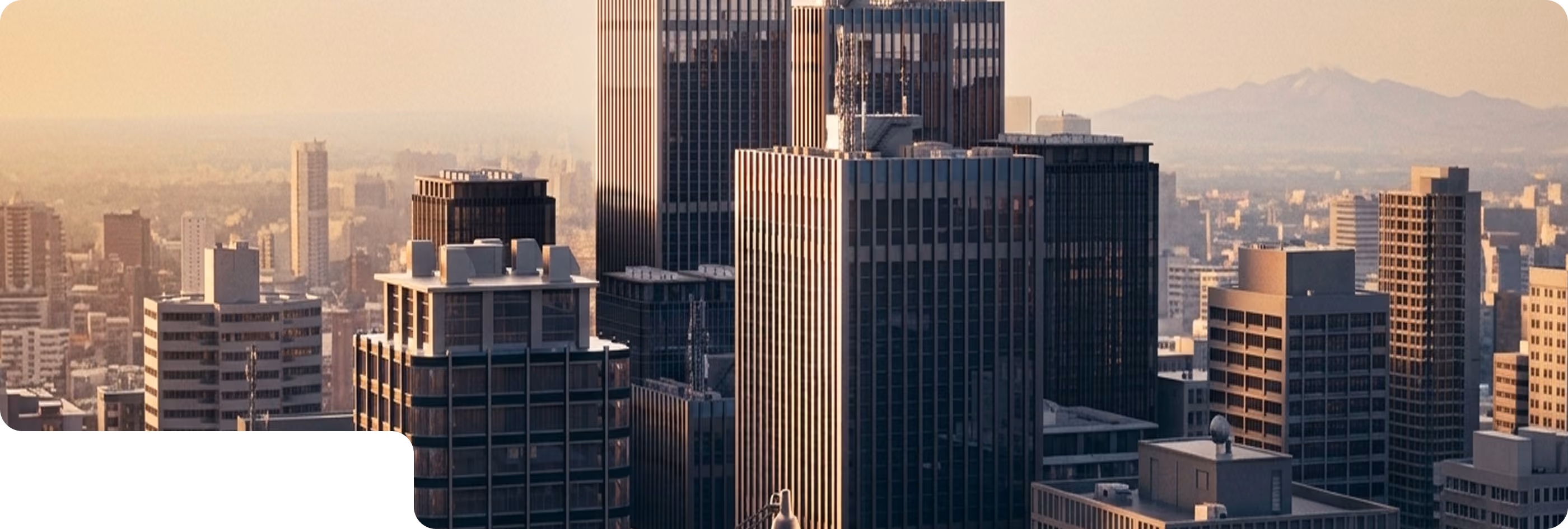 View of a city skyline at sunrise or sunset with tall buildings and mountains faintly visible in the background under a soft sky.