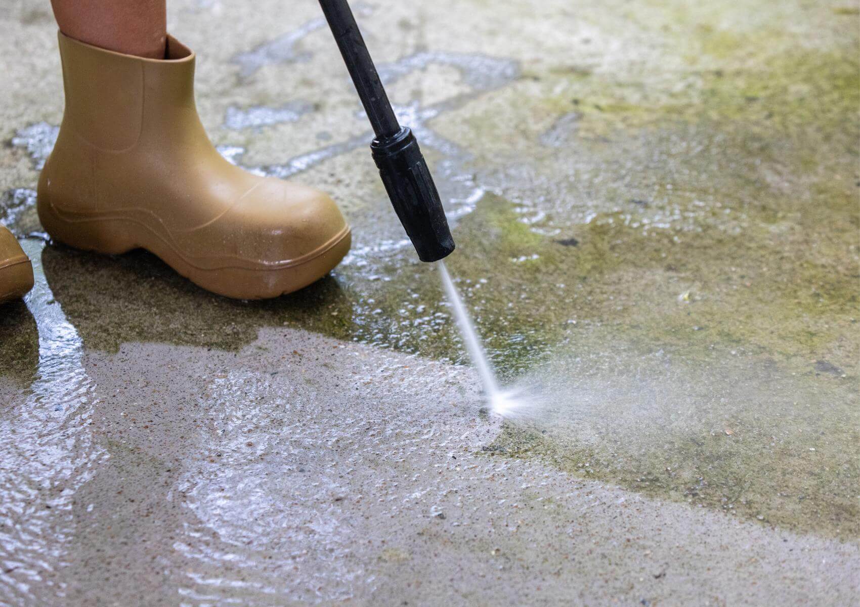 worker cleaning concrete pavement using high pressure washer