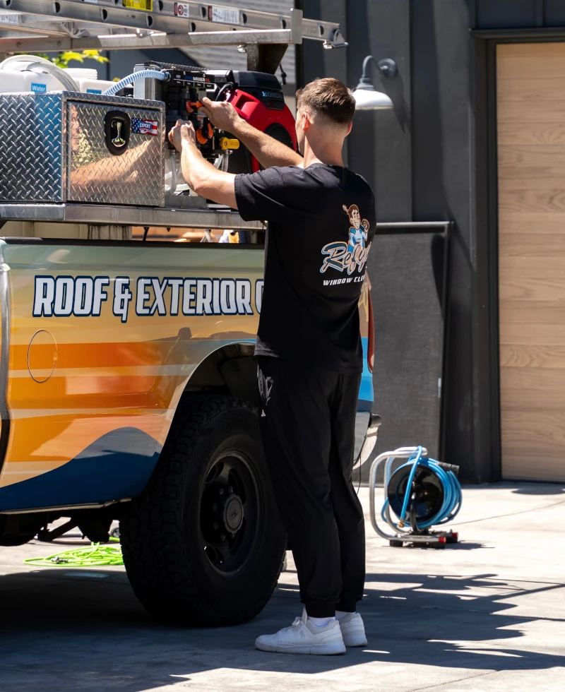Refyne technician adjusting pressure washing equipment mounted on a Roof & Exterior Cleaning service truck