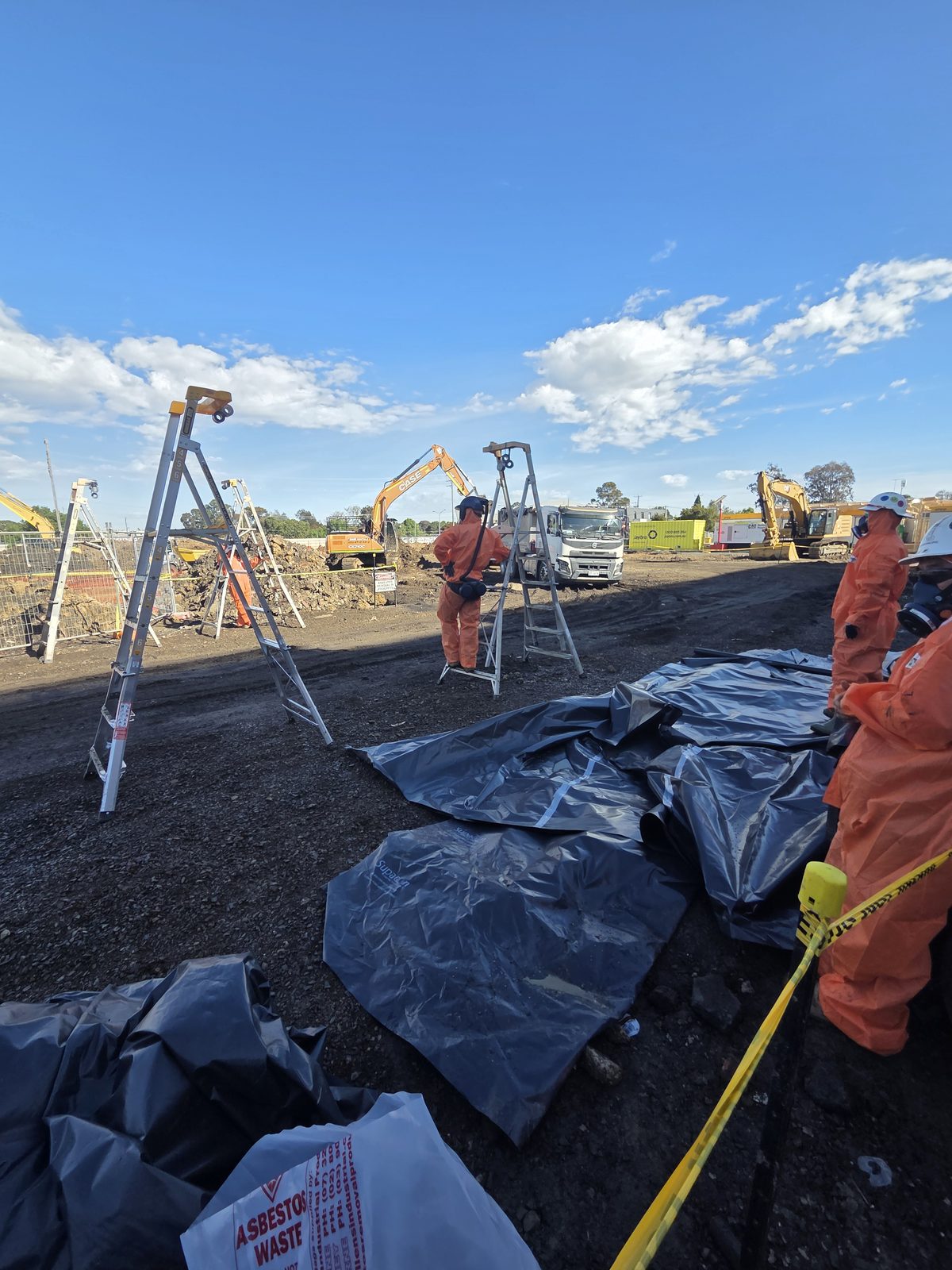 Workers in protective suits beside covered stockpiles