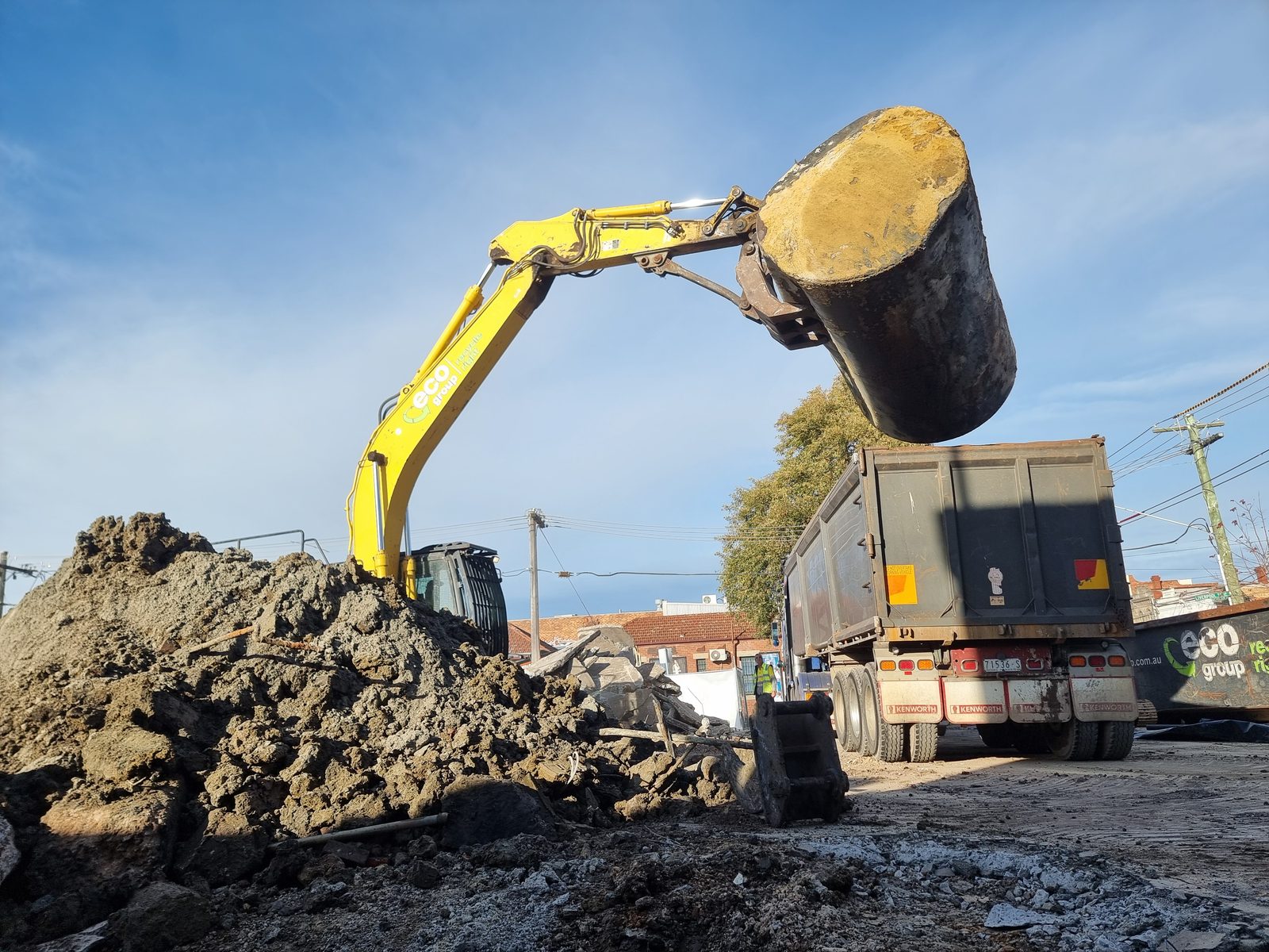 Excavator lifting a storage tank beside a truck